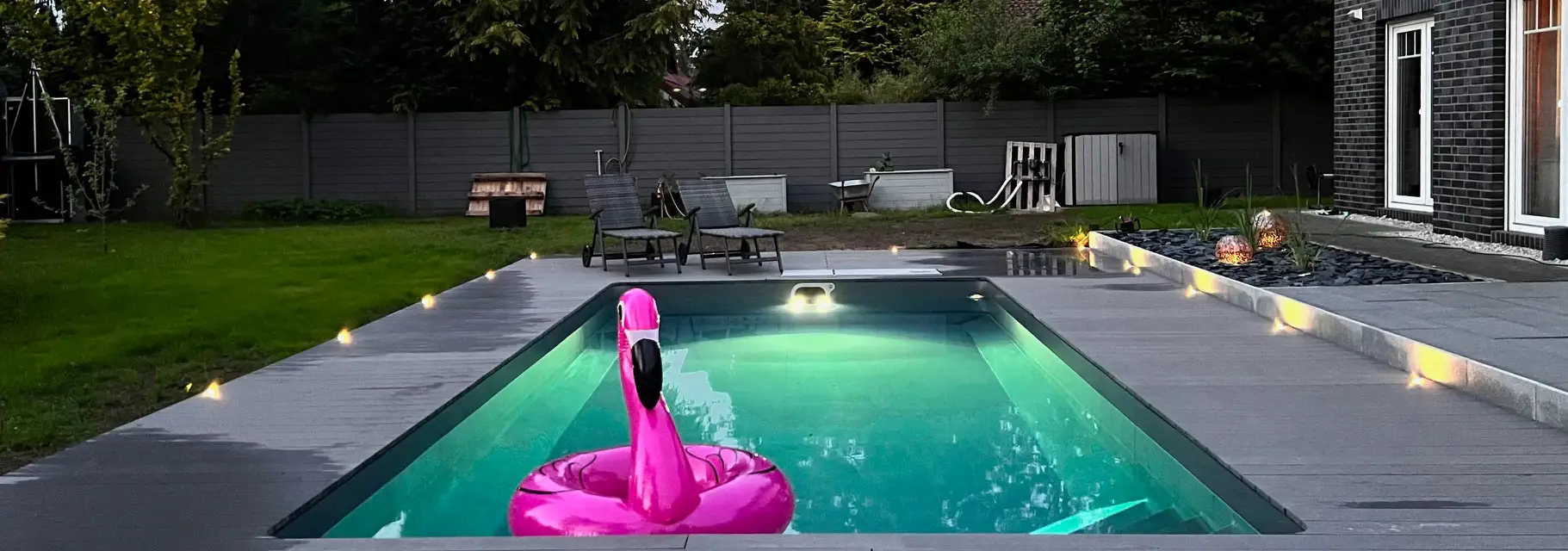 Swimmingpool bei Nacht mit Poolbeleuchtung und Flamingo